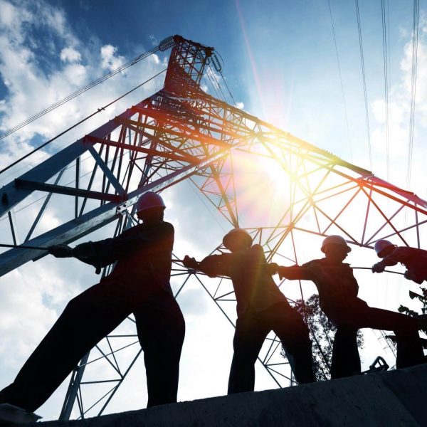 Workers silhouetted against a power transmission tower, demonstrating teamwork in construction and renovation projects.