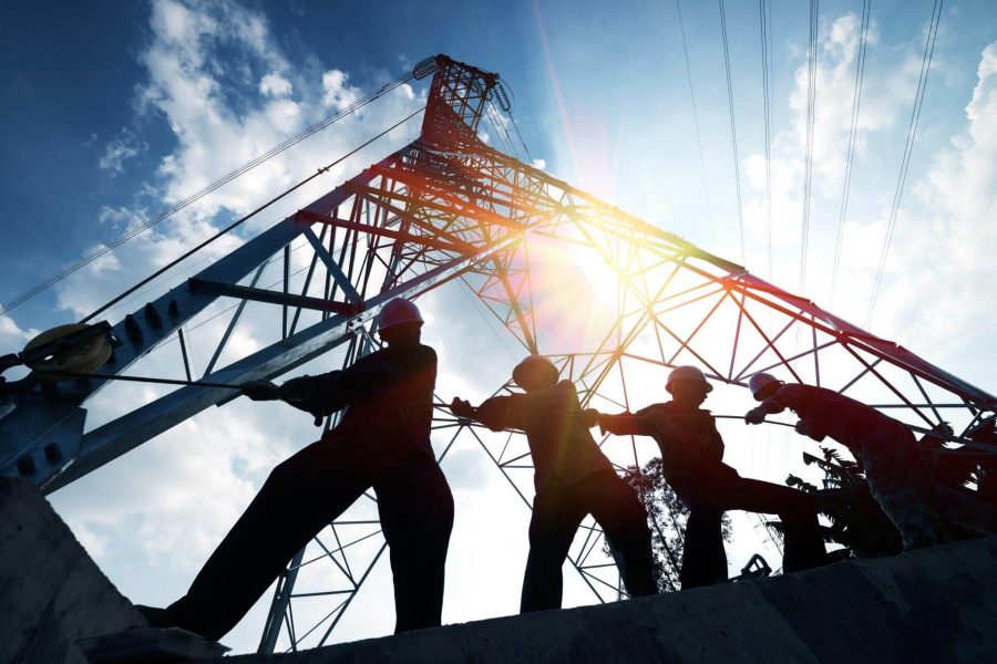 Construction workers pulling cable near a tall steel structure against a bright sky, representing building renovation and construction efforts by RH Remodeling.
