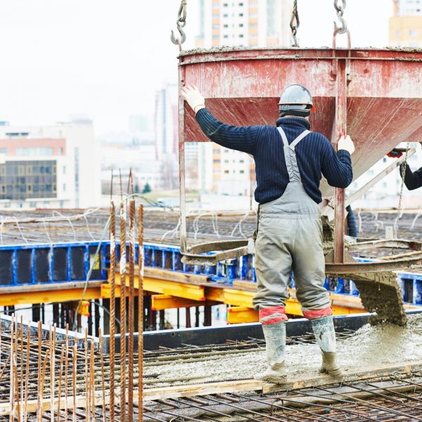 Construction worker operating a concrete mixer on a building site, surrounded by rebar and scaffolding, showcasing public building renovation efforts.