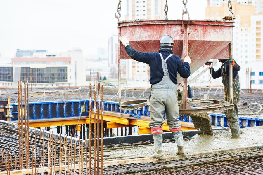 Construction workers pouring concrete from a large mixer on a building renovation site, showcasing structural elements and urban backdrop.