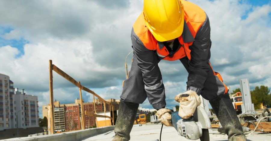 Construction worker in safety gear using a power tool on a concrete slab at a building site, showcasing RH Remodeling's expertise in construction and renovation services.